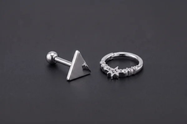 Silver triangular ear stud beside a decorative cartilage hoop