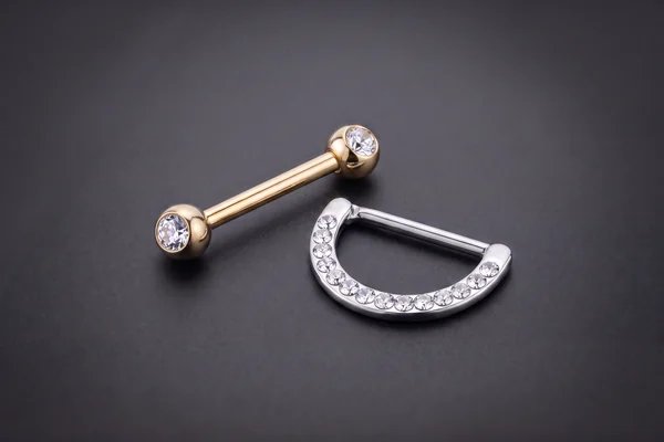 Gold gemstone-ended barbell beside a silver jewelled nipple clicker
