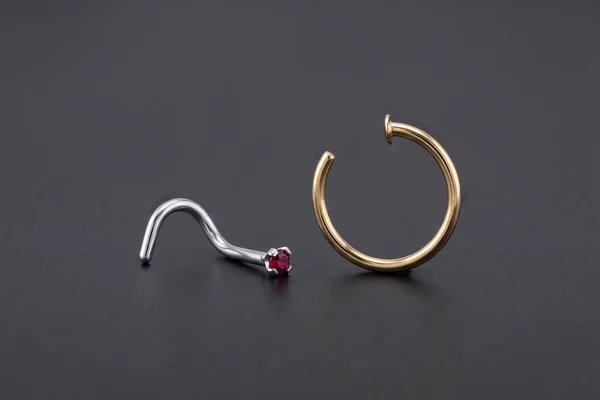 Silver red gemstone nose stud beside an open gold nose ring