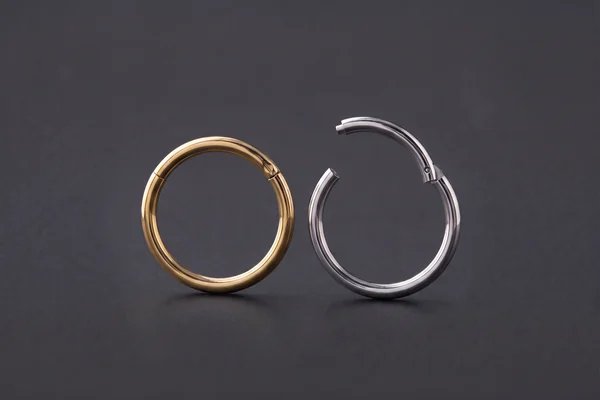 Closed gold hinged ring beside an open silver clicker